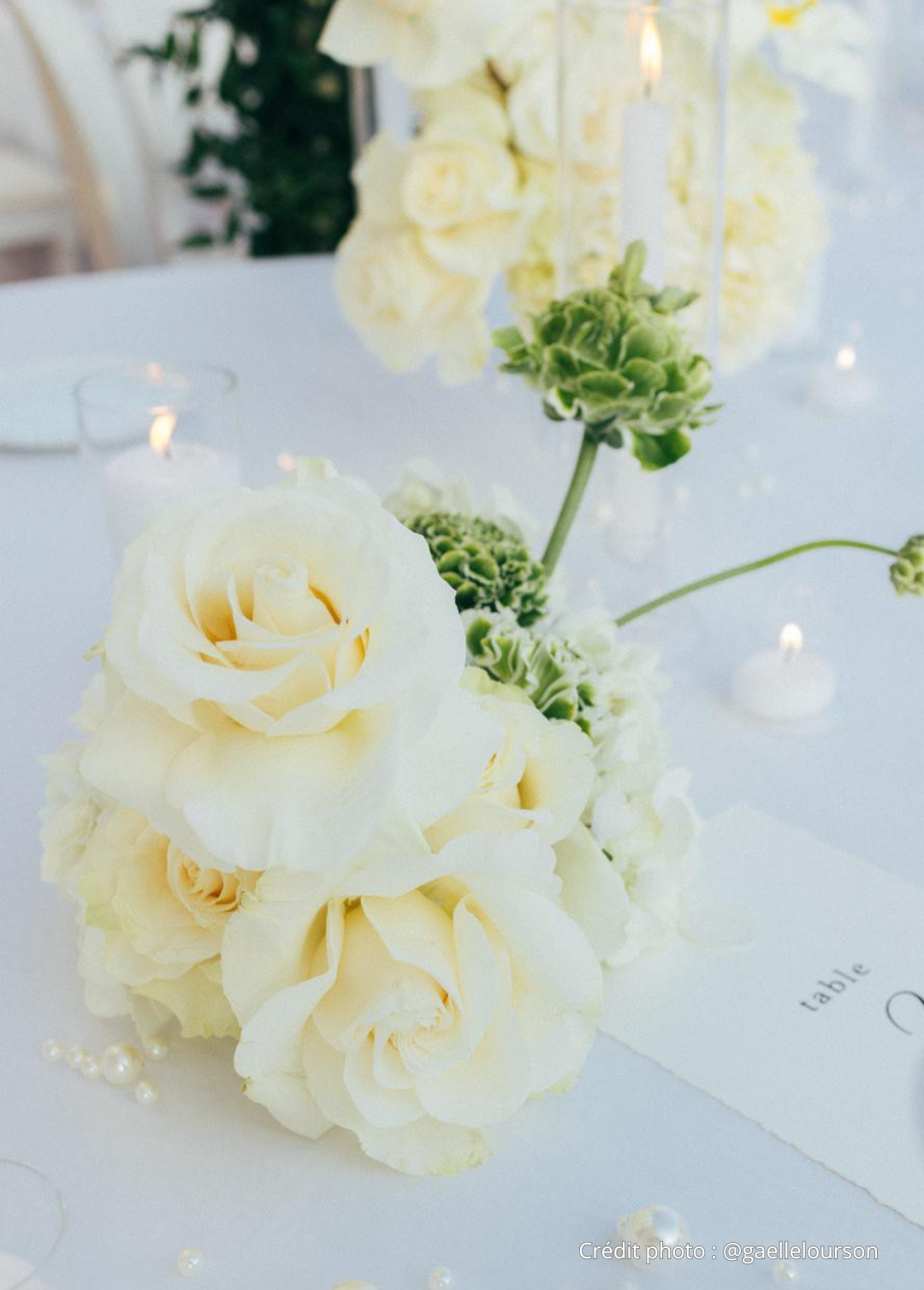 Centre de table floral avec des roses blanches, des fleurs vertes, des bougies et des perles, en décor de mariage élégante
