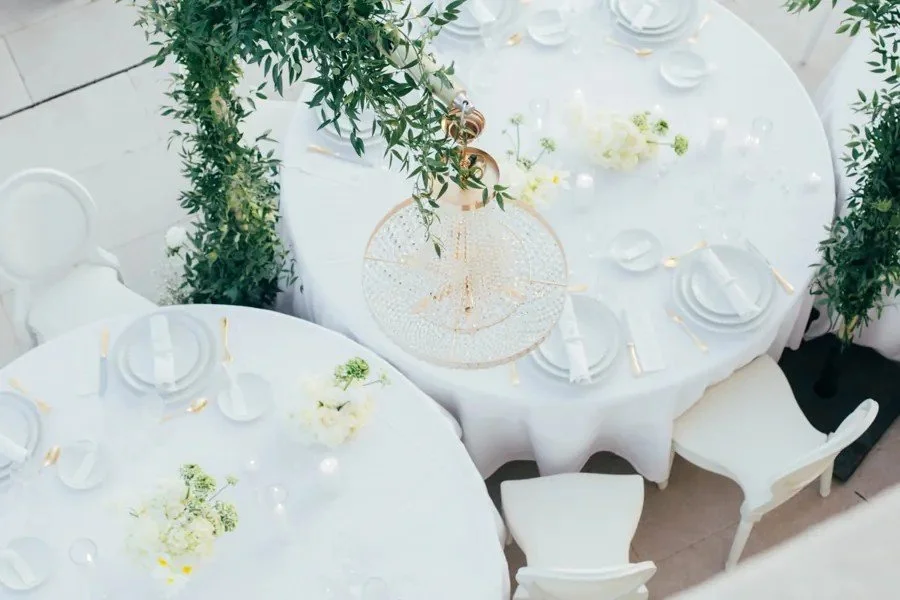 Vue du dessus : tables rondes blanches, lustre en cristal et arche de verdure.