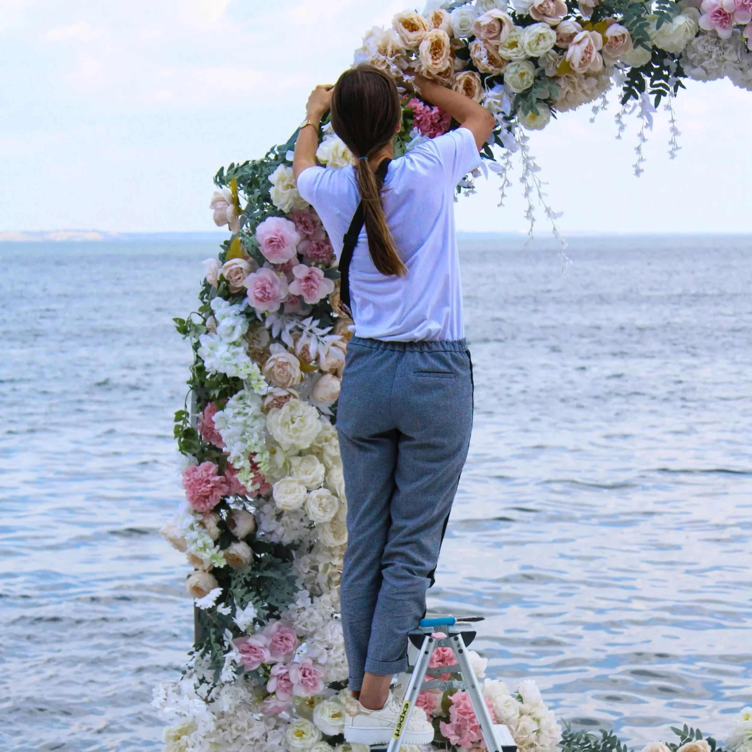 Une personne ajuste une structure florale près de la mer.