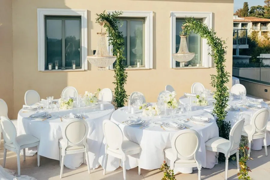 Tables rondes nappées de blanc et chaises médaillon blanches sur une terrasse.