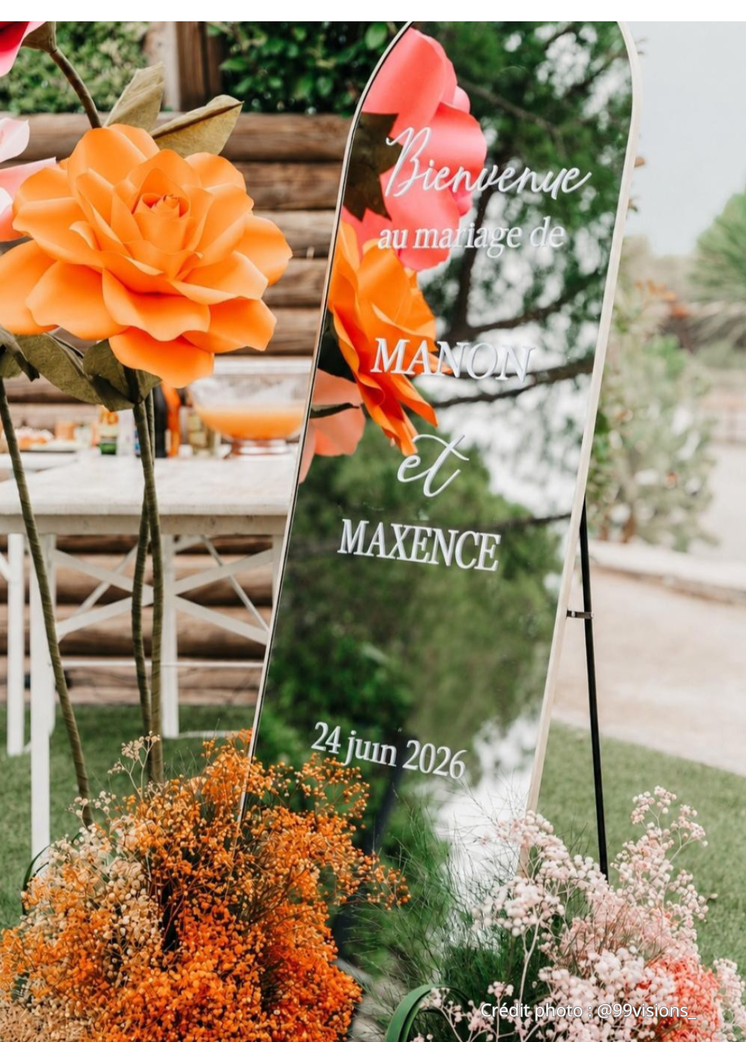 Décoration florale de mariage avec un miroir triptyque et des fleurs orange et roses, en extérieur.