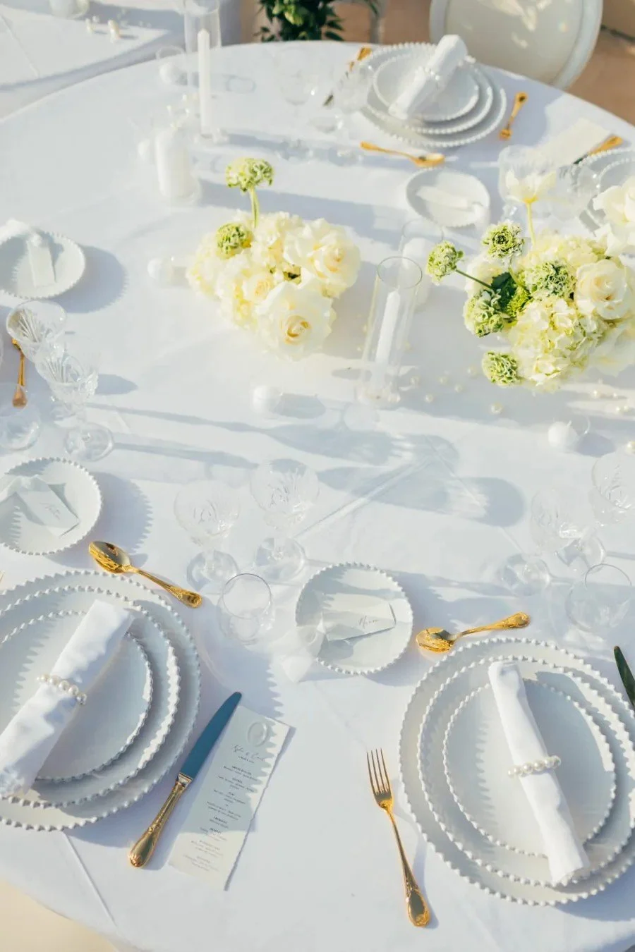 Table de réception blanche, compositions de roses et d’hortensias, vaisselle perlée et couverts dorés.