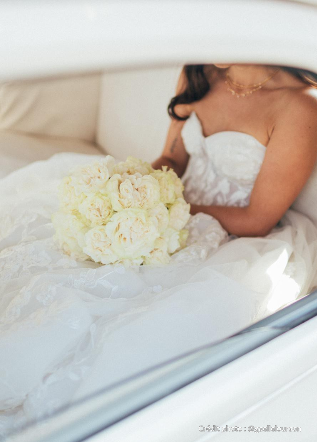 Une femme en robe de mariage blanche tient un bouquet de fleurs blanches dans une voiture.