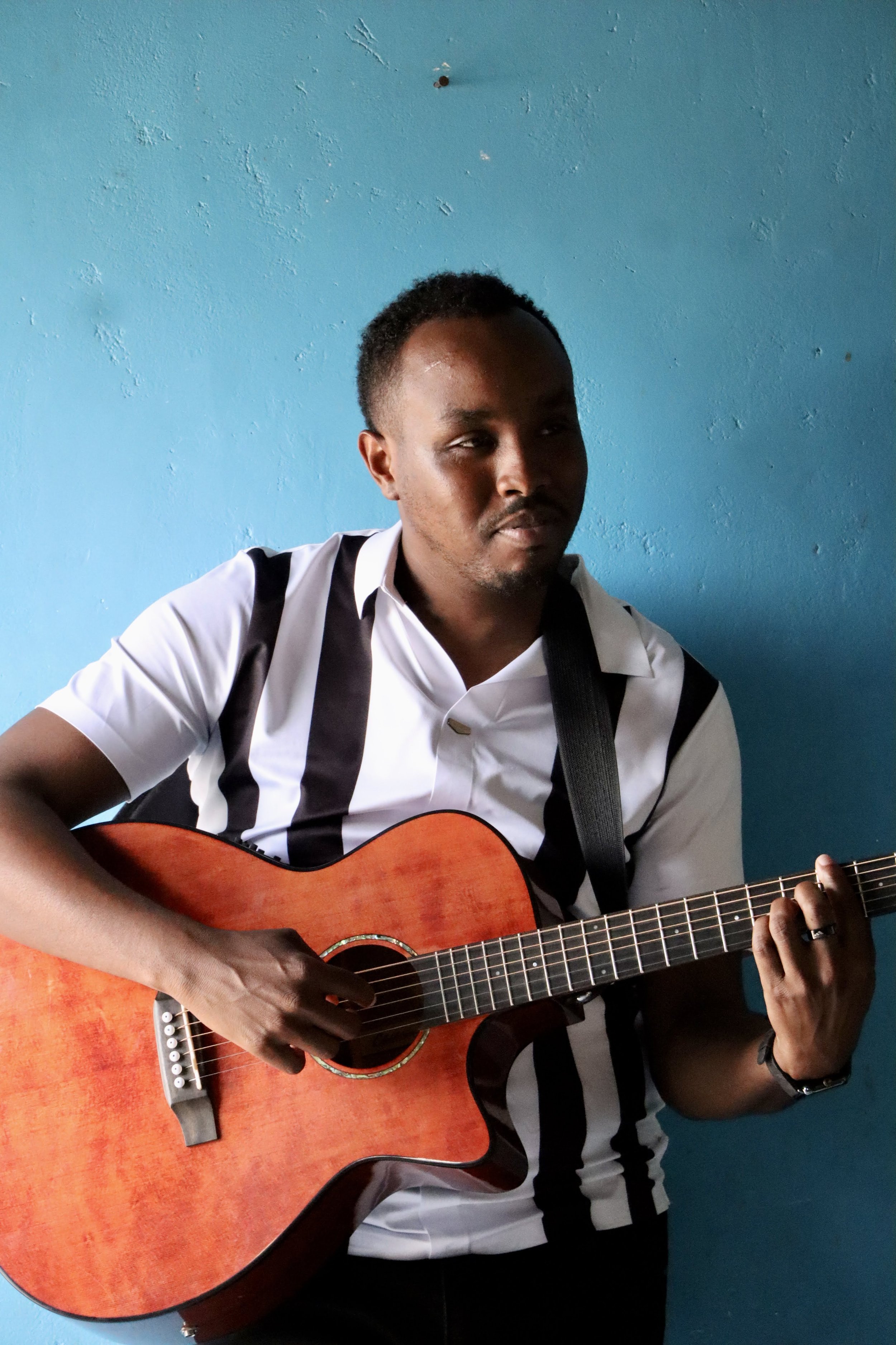 A man playing an acoustic guitar against a blue wall.