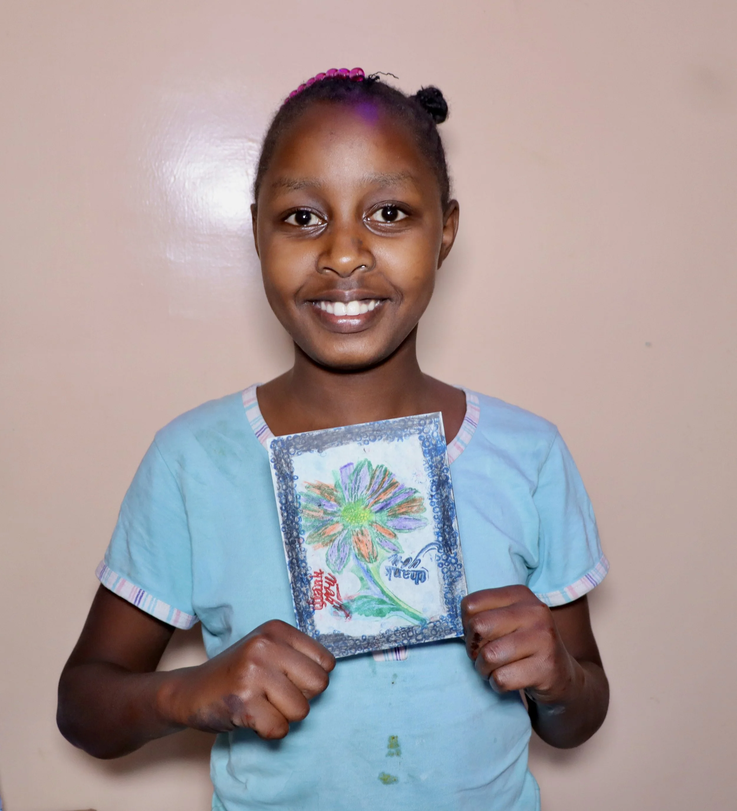 A smiling girl holding a colorful drawing of a flower on paper.