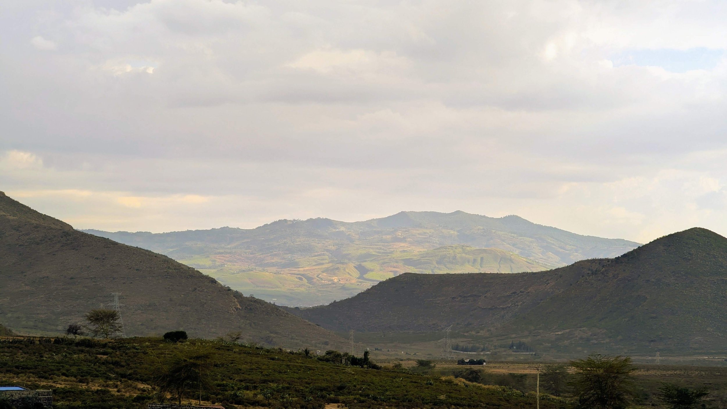 Scenic landscape of rolling hills and mountains with partly cloudy sky.