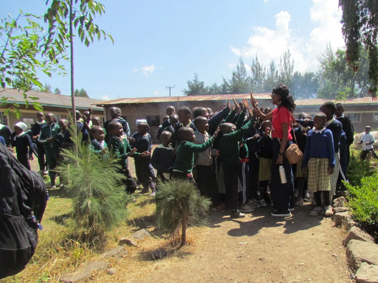A group of school children giving high fives to a woman outside on a sunny day.