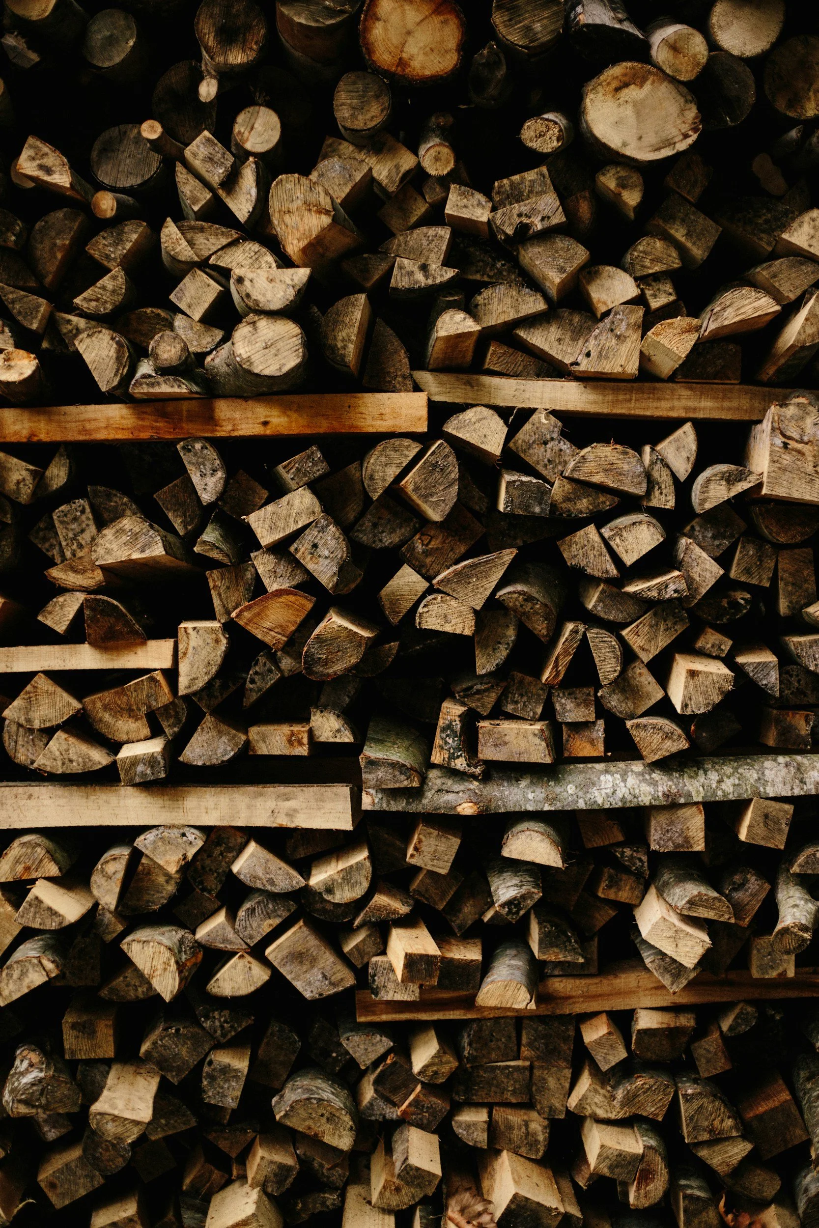 Stacked cut firewood logs of various sizes and shapes, arranged horizontally.