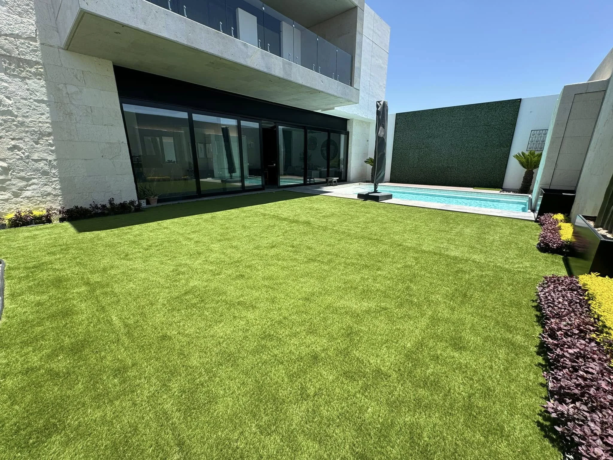 Patio de una casa moderna con césped, piscina en el fondo, paredes blancas y macetas con plantas decorativas