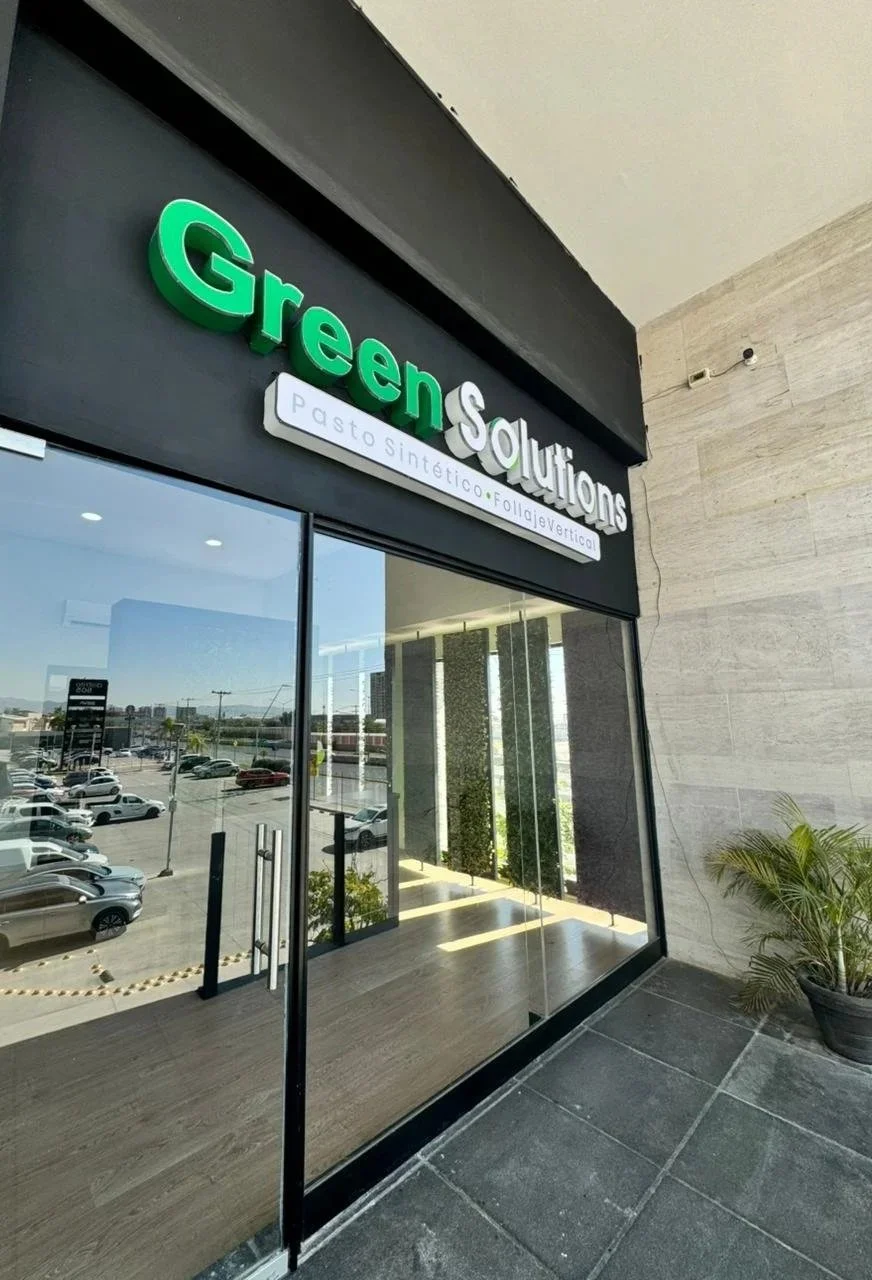 Entrada de una tienda llamada Green Solutions con un letrero que dice 'pasto sintético folia vertical'.
