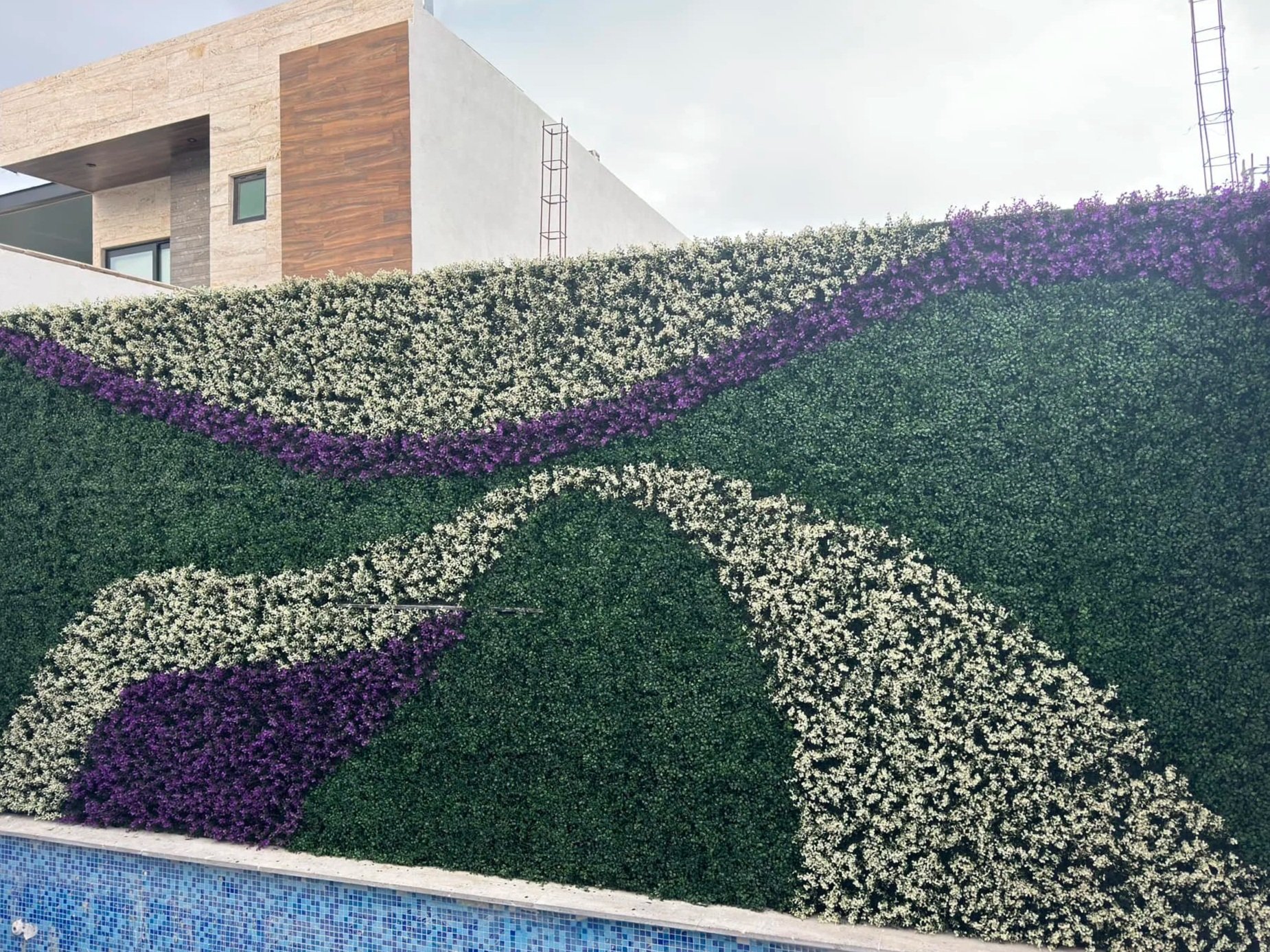 Muro decorativo con diseño de flores blancas y moradas en forma de mariposa, con edificio moderno al fondo.