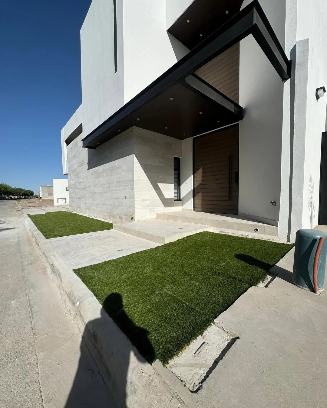 Fachada moderna de casa con entrada principal de madera, porches y áreas verdes.