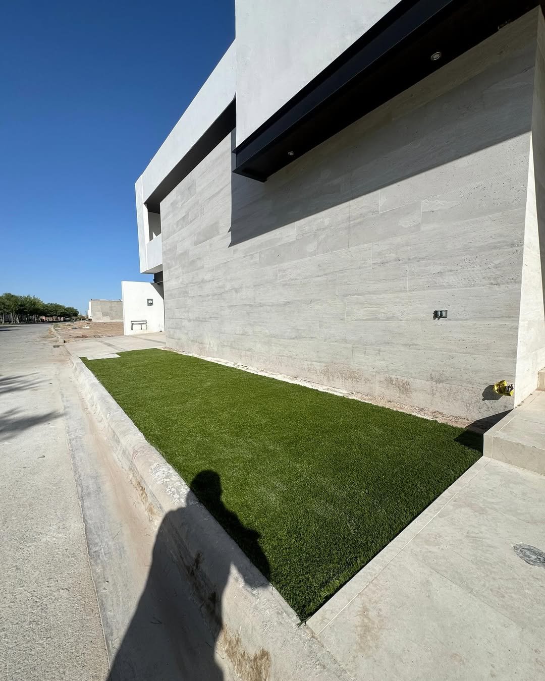 Fachada moderna de un edificio con muro de concreto y un área pequeña de césped verde.