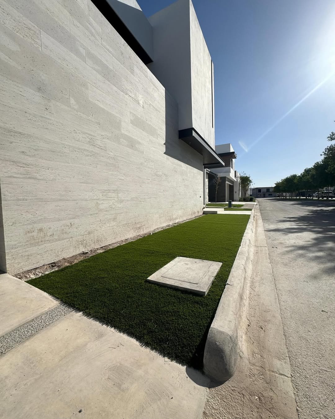Vista lateral de un edificio moderno con paredes de concreto y áreas de césped bien cuidado, en un día soleado con cielo despejado.