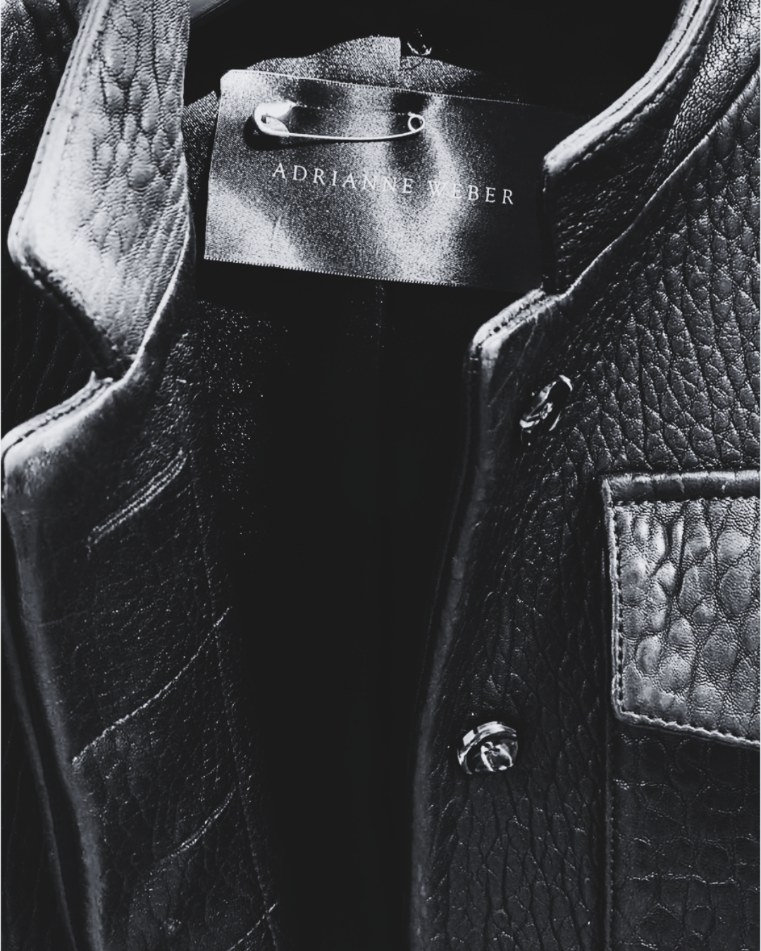 Close-up of a black leather bag's interior with a clothing tag that reads 'AdriAnne Weber'.