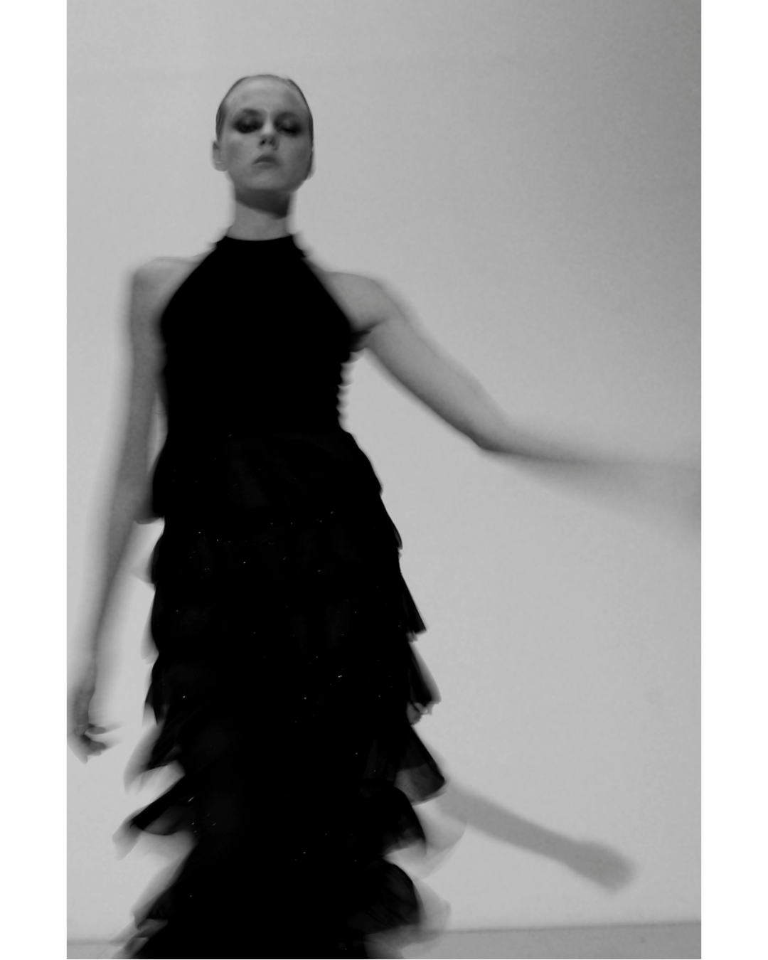 A woman in a black dress standing against a plain wall, with a blurred motion effect.
