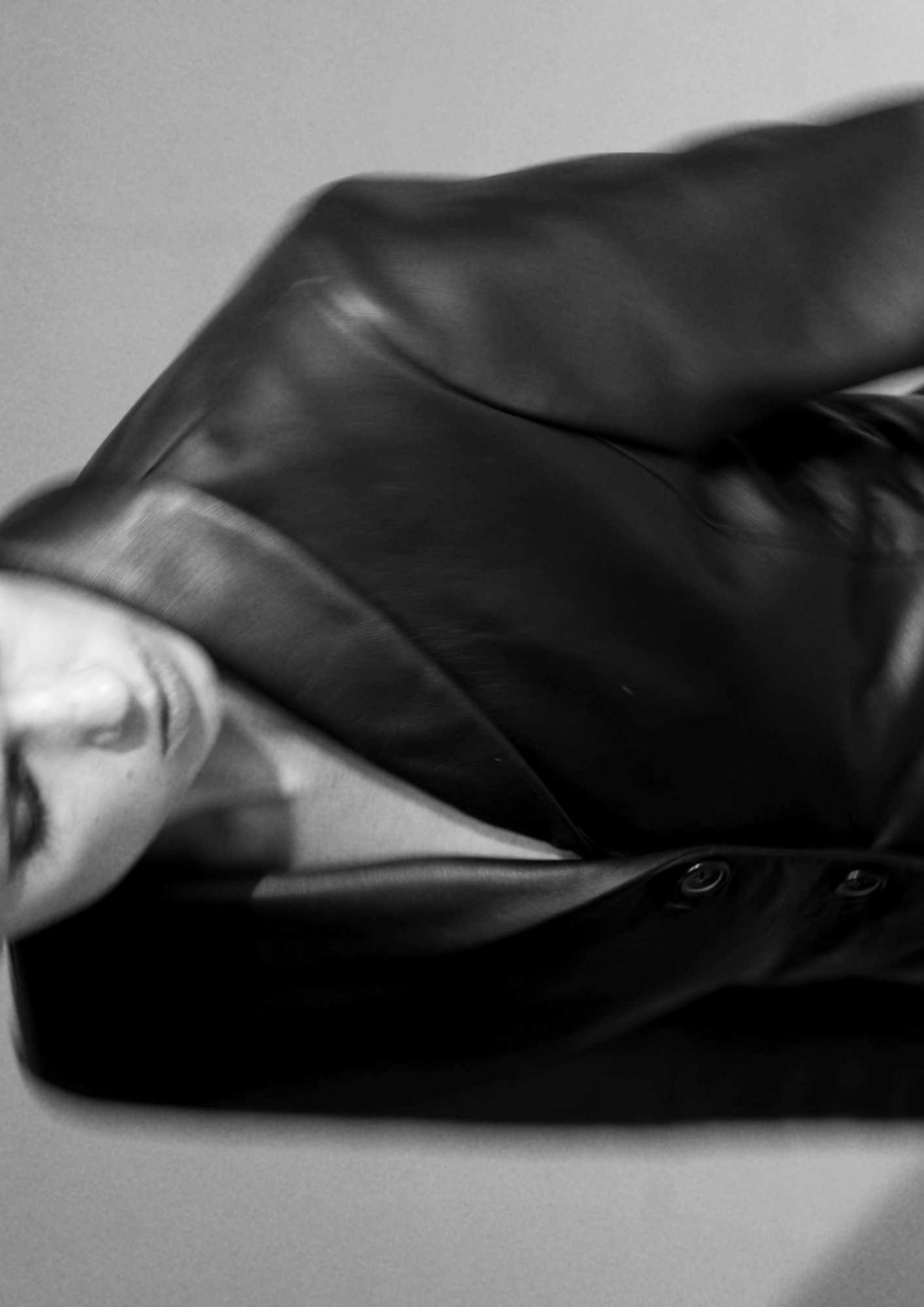 Black and white close-up of a person's face partially obscured, wearing a leather jacket with the collar turned up.