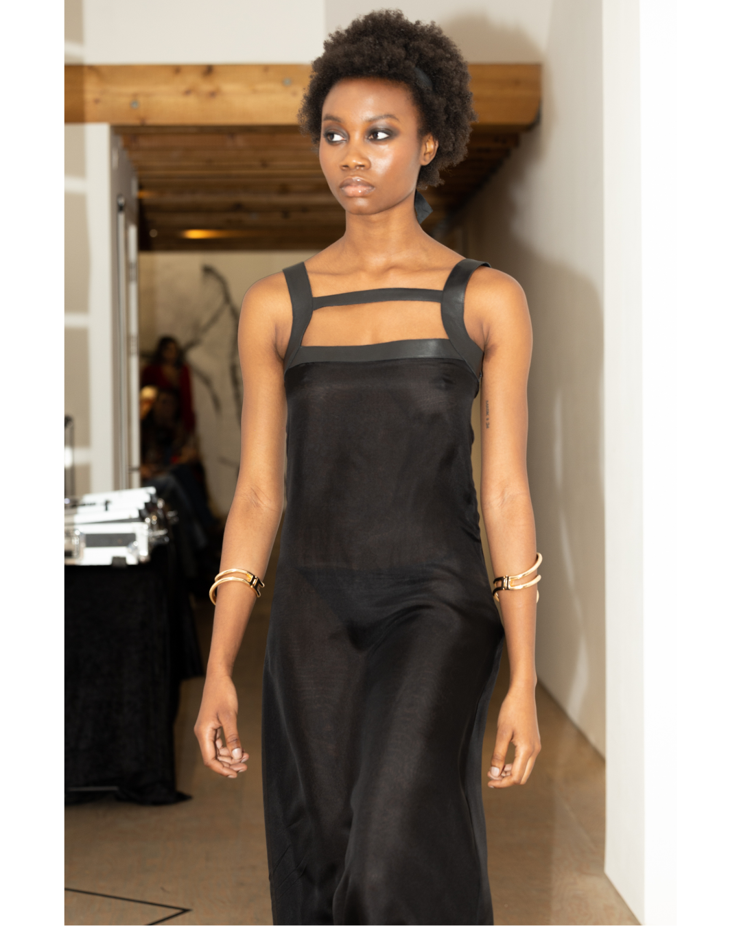 A woman walking down a runway wearing a black sleeveless dress with cut-out details on top.