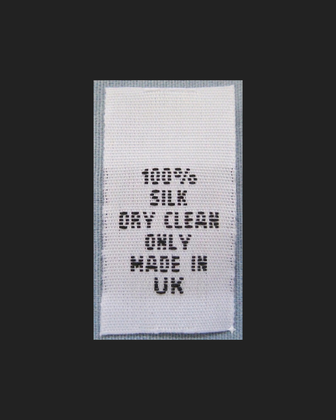 White textile label with black stitched text reading "100% SILK DRY CLEAN ONLY HAND IN UK" against a dark background.