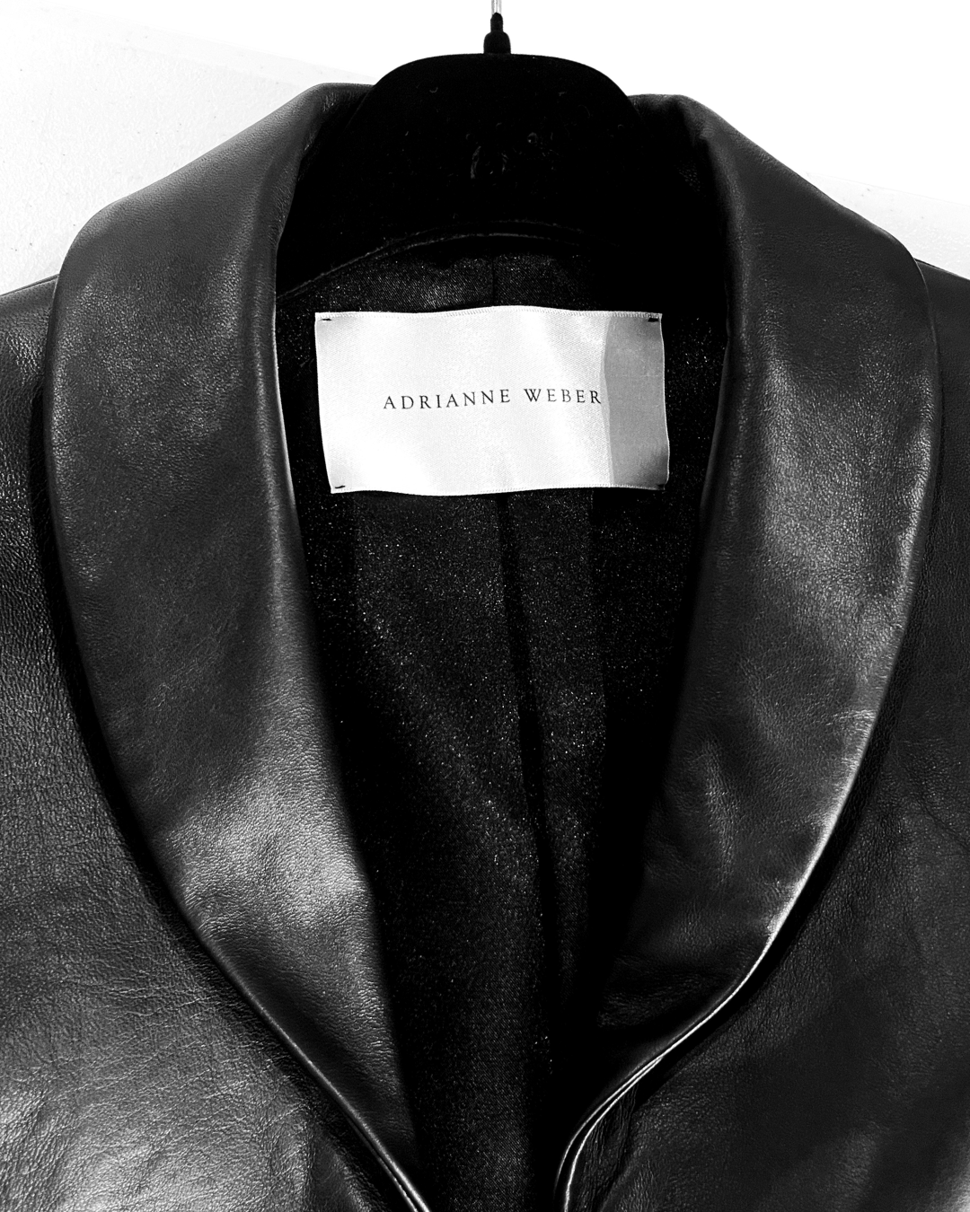 Close-up of a black leather jacket with a white label that reads 'Adrianne Weber' inside the collar.