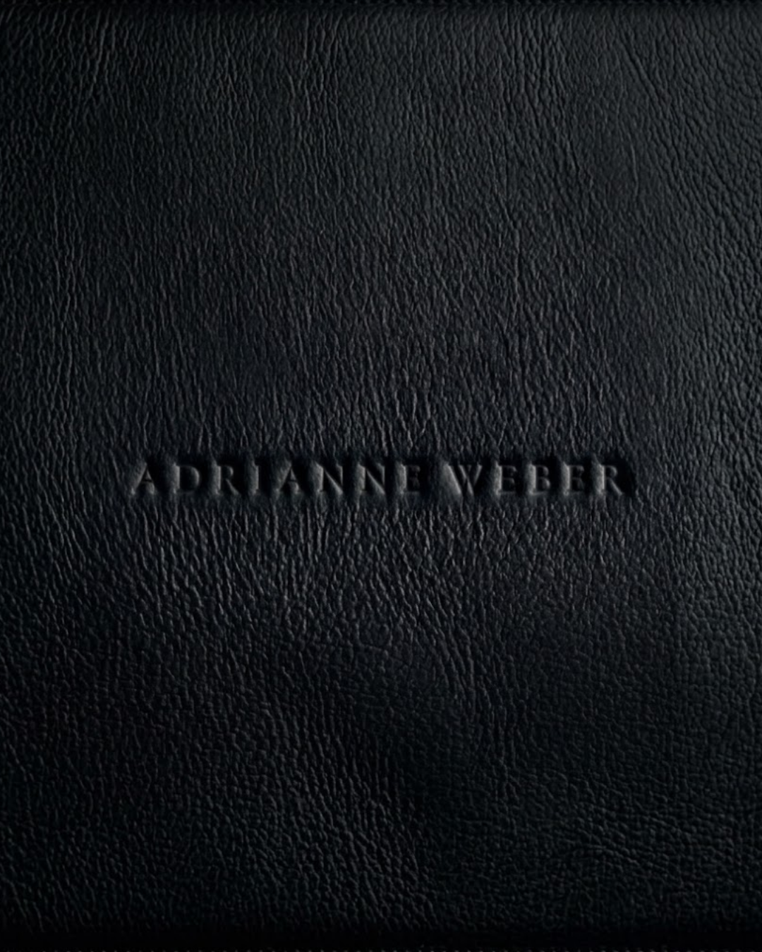 Black leather surface with engraved text 'Adriane Weber'.