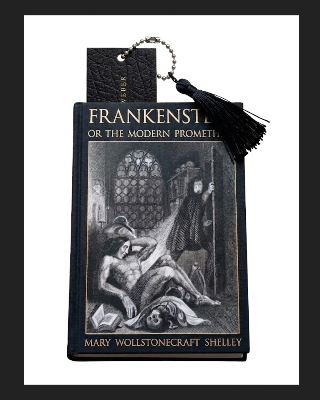 A hardcover book titled 'Frankenstein or The Modern Prometheus' by Mary Wollstonecraft Shelley, with a bookmark, a black tassel, and a small black leather cardholder or tag resting on top.