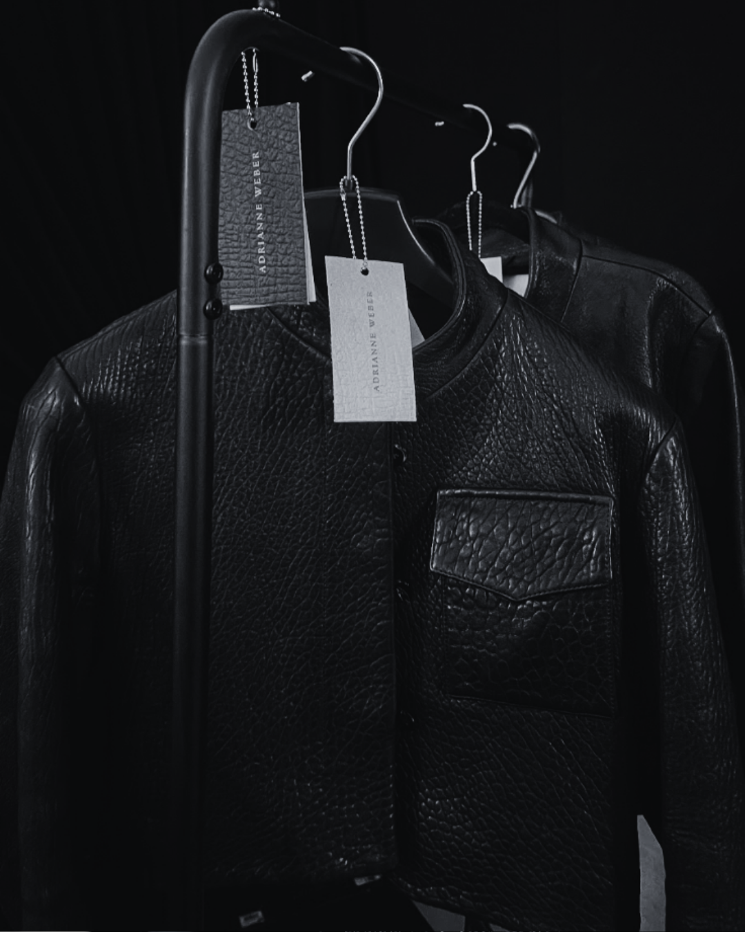 Black leather jacket on a hanger with tags, hanging on a black clothing rack
