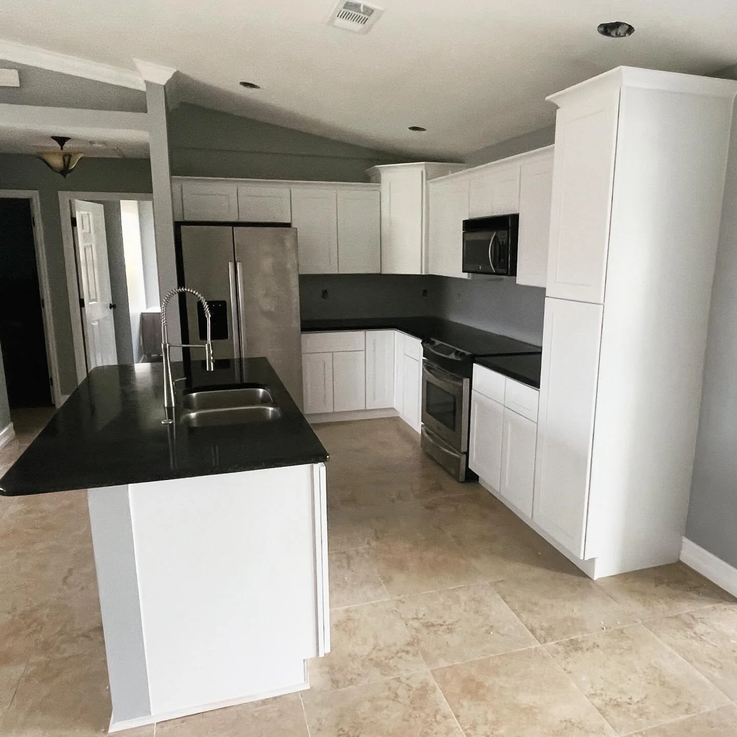 A modern kitchen with white cabinets, black countertops, stainless steel appliances, and a large island with a double sink.