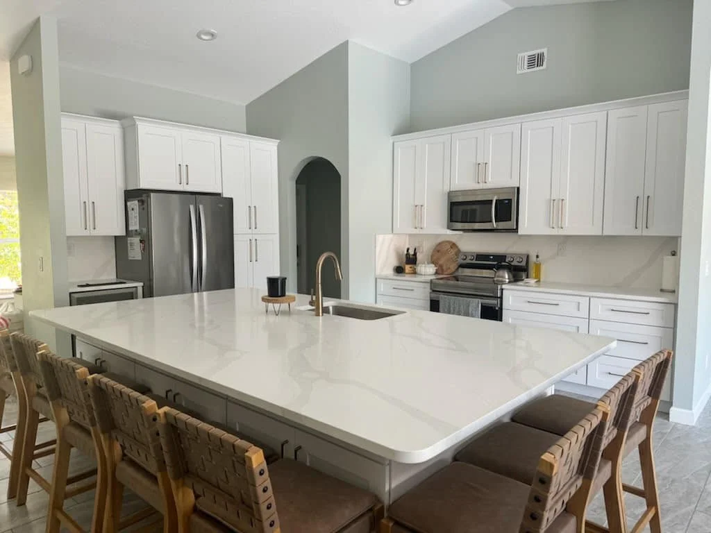 Modern kitchen with white cabinets, stainless steel appliances, a large white island with seating, and light-colored walls.