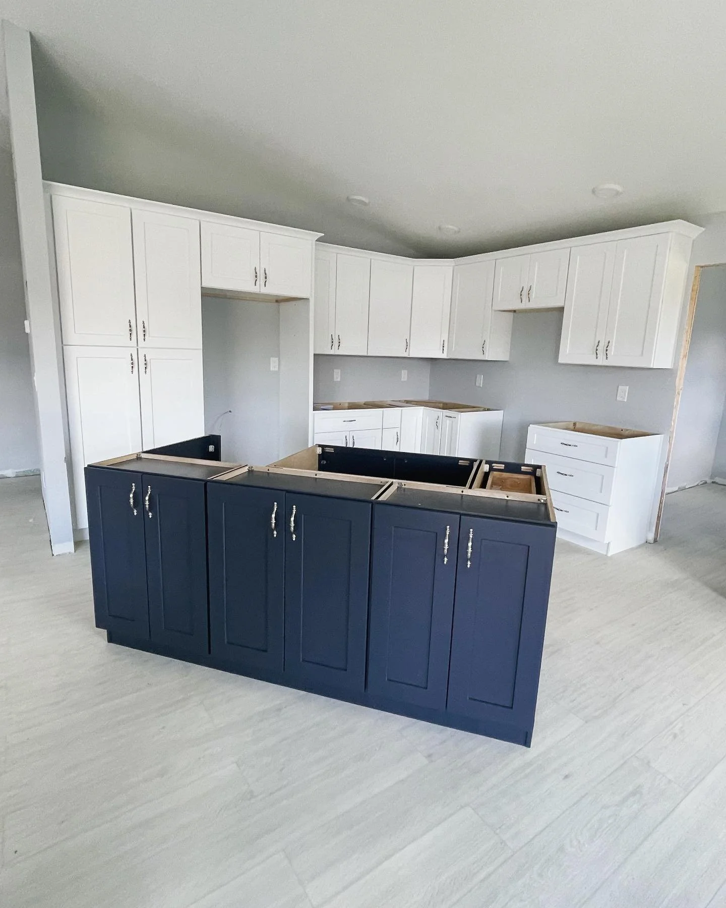 Kitchen under construction with white upper cabinets and a dark blue lower island cabinet. The countertops are not yet installed.