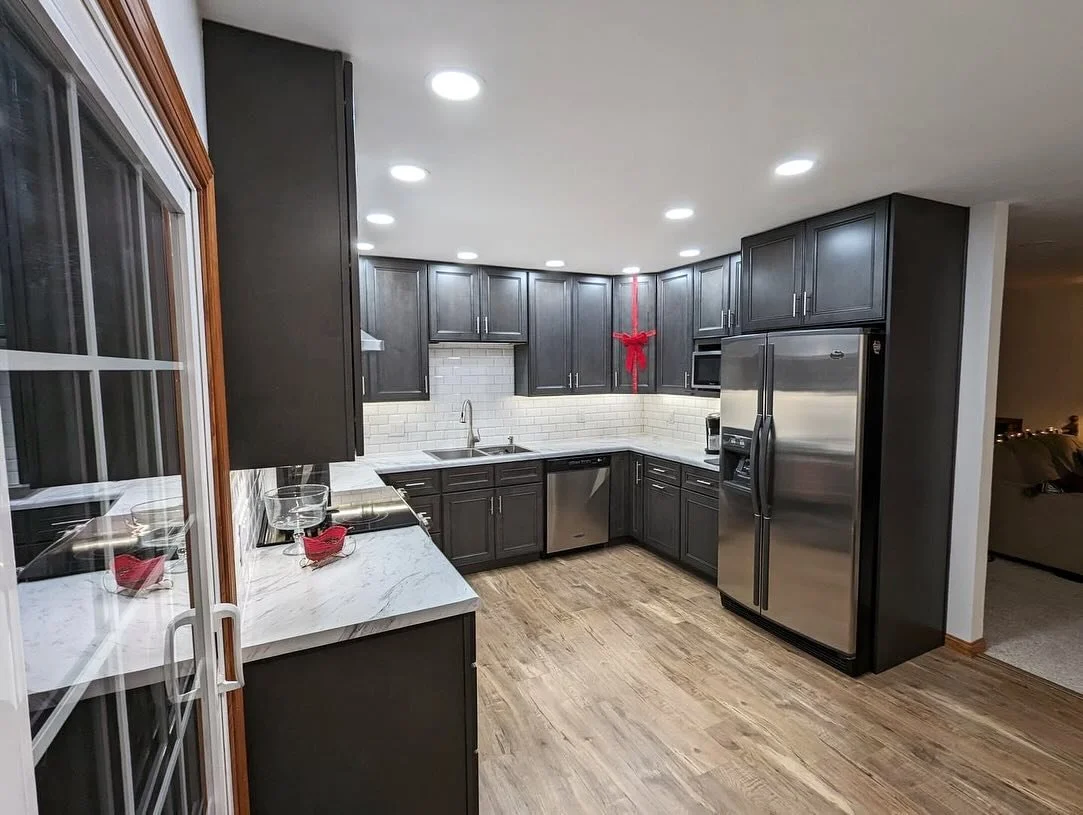 Modern kitchen with dark cabinets, white subway tile backsplash, stainless steel appliances, and wooden flooring.