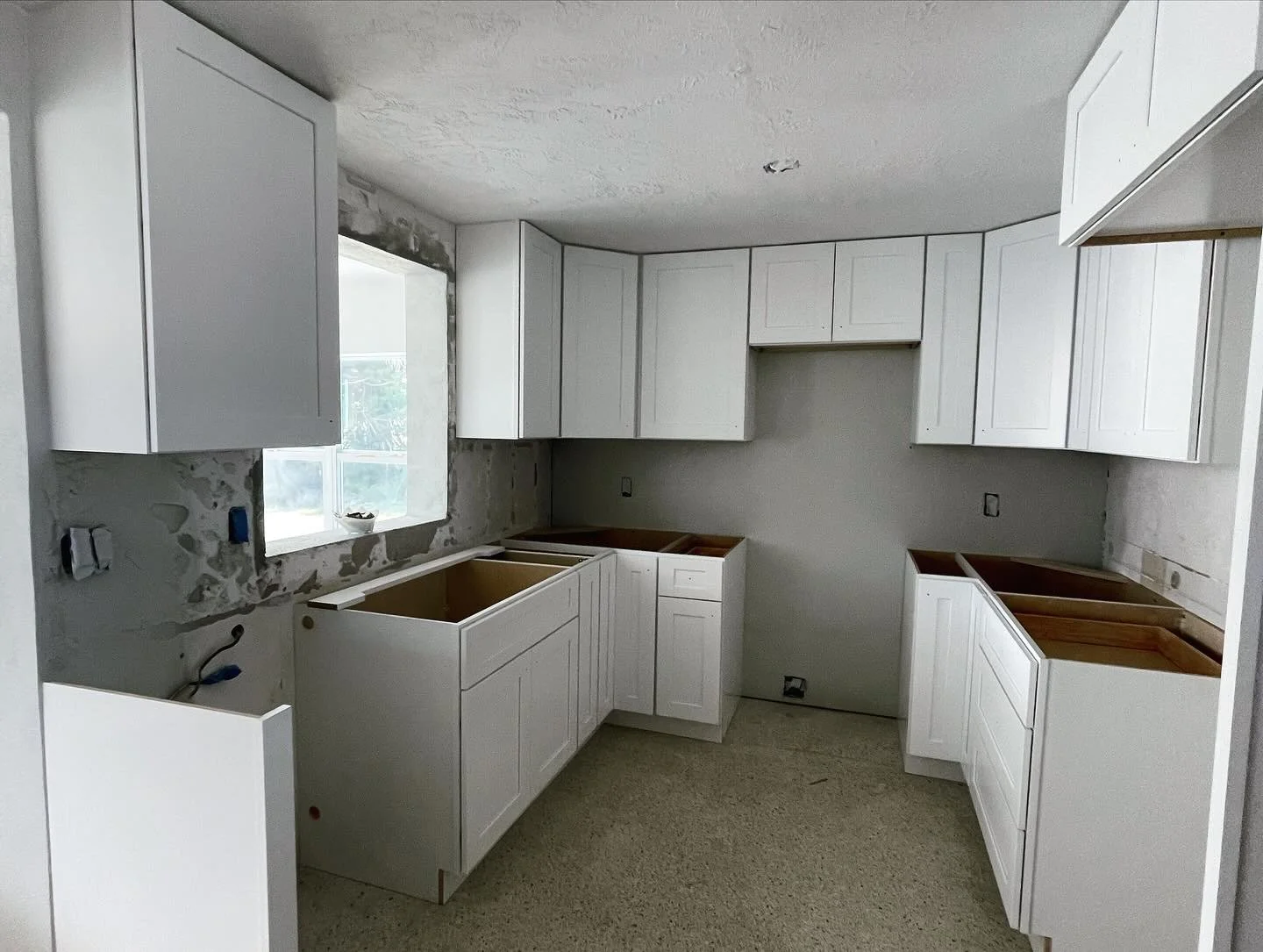 Kitchen under construction with white cabinets, no countertops installed, and a window providing natural light.