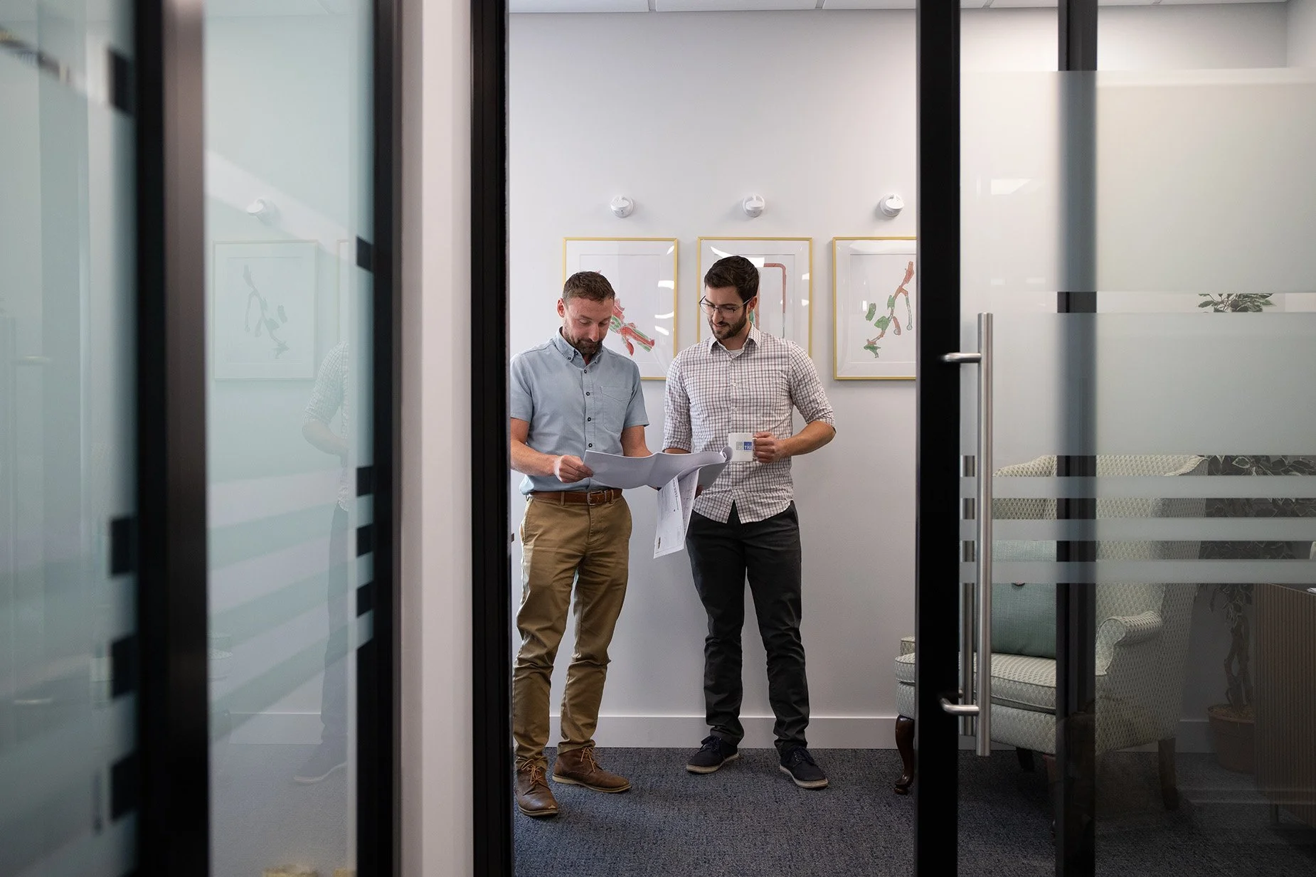 Two men standing in an office, reviewing documents and having a discussion.