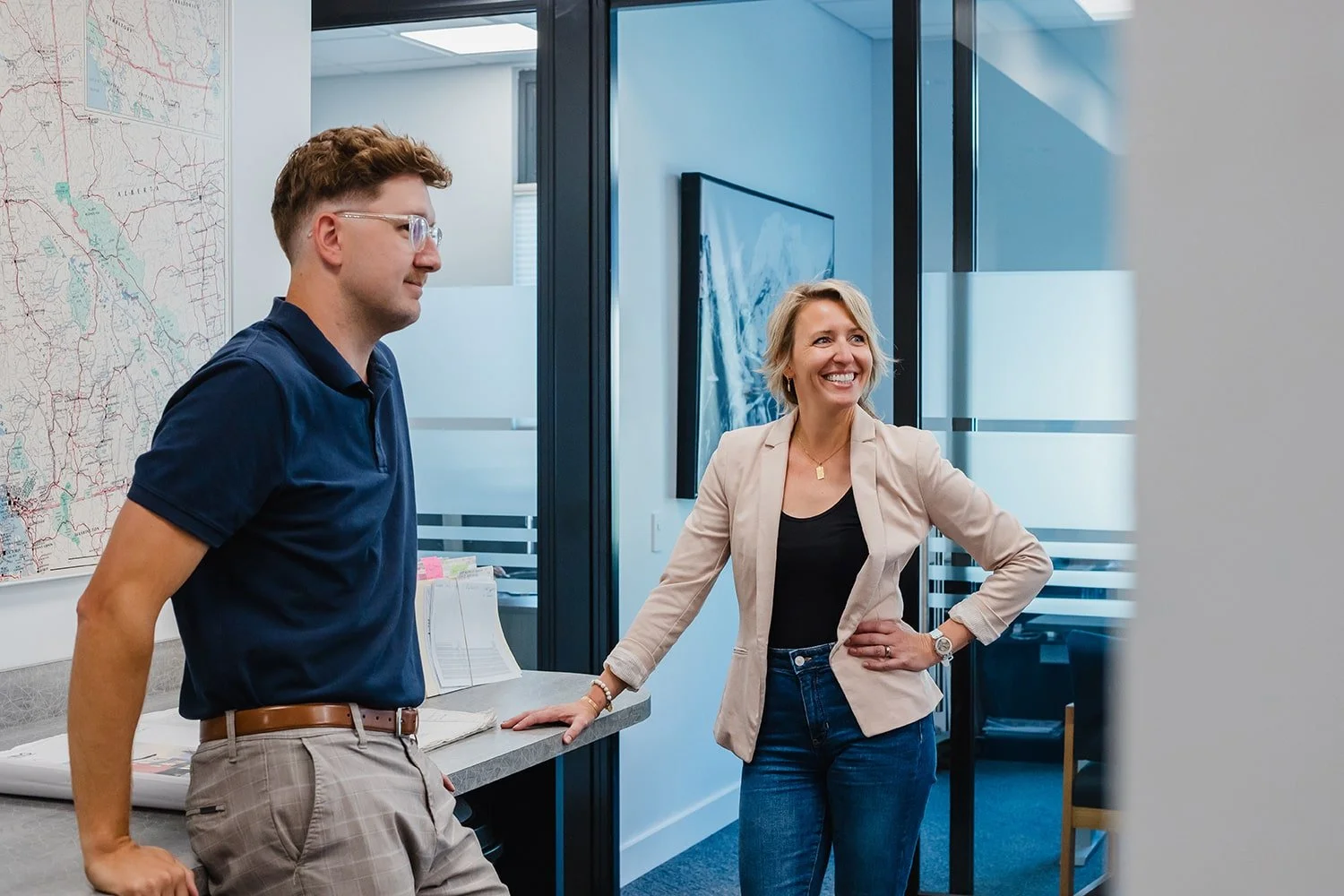 Two colleagues, a man and a woman, in an office, smiling and talking.