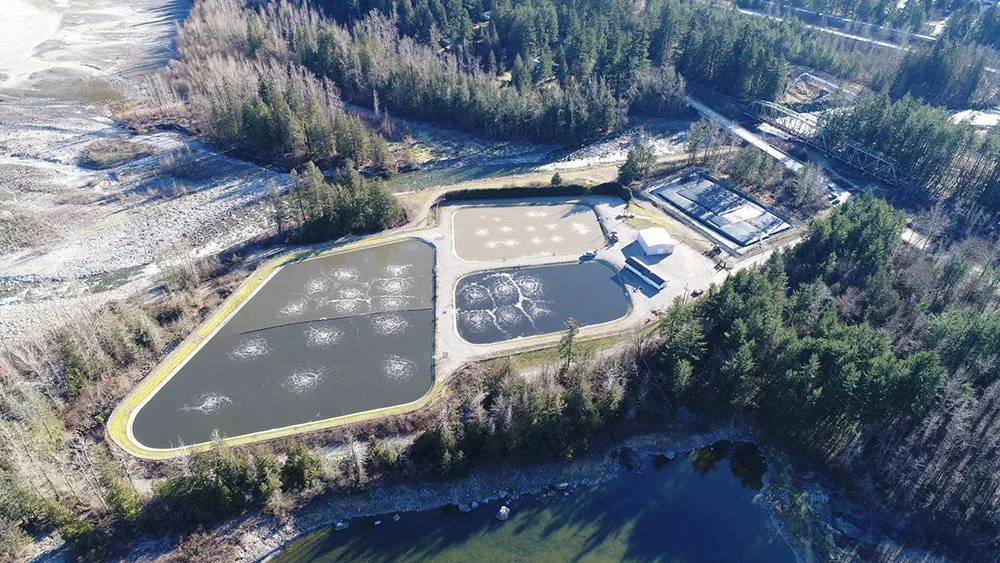 Aerial view of a wastewater treatment plant surrounded by trees and a river.