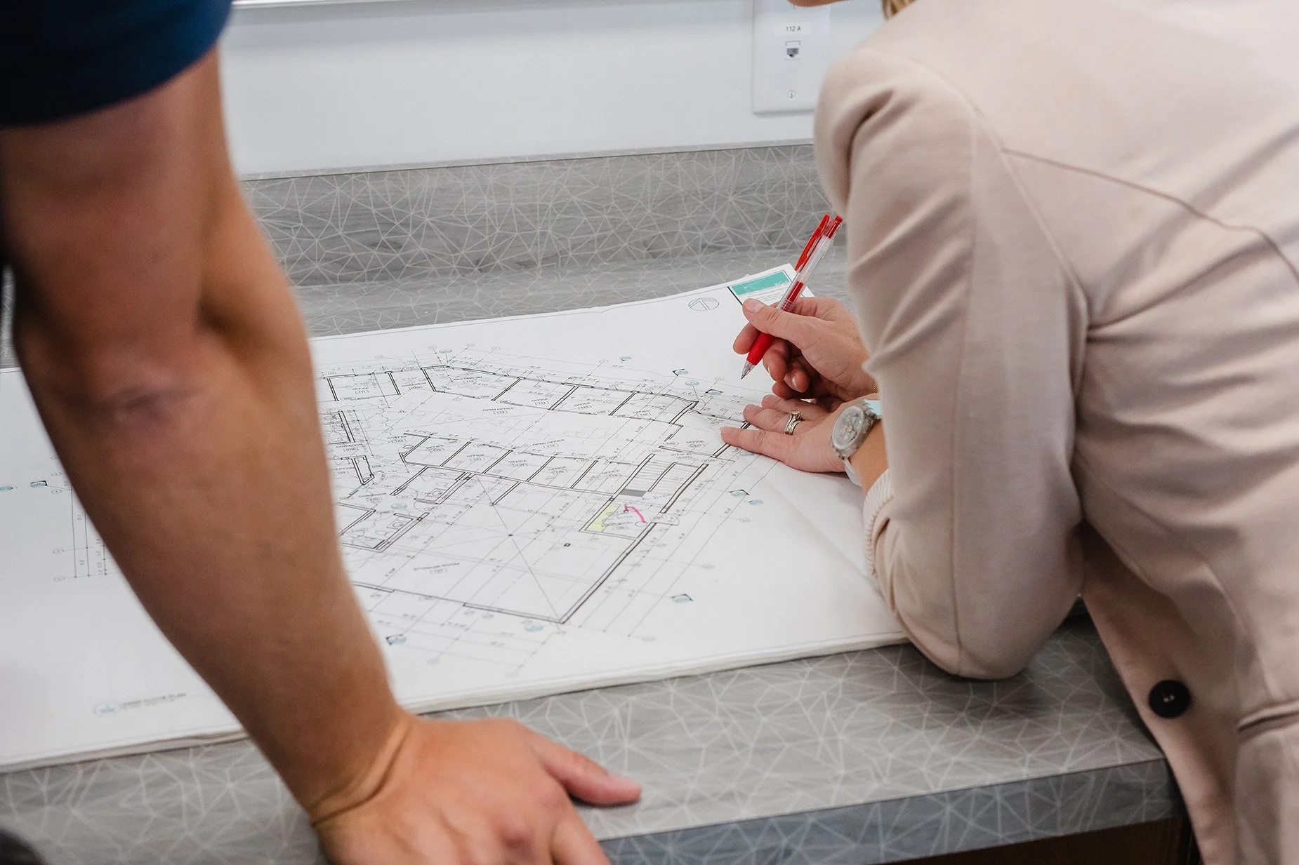 Two people examining architectural blueprints on a table.