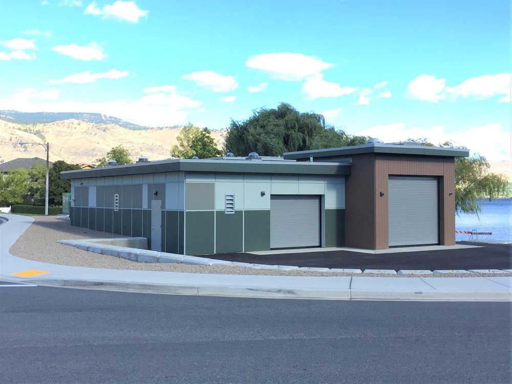 A modern building with two garage doors, located near a body of water, with mountains and blue sky in the background.