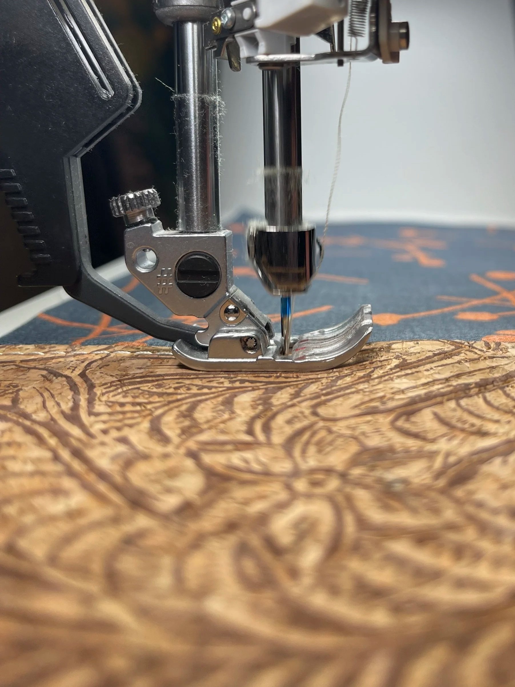 Close-up of a sewing machine needle stitching a pattern on brown wood-textured fabric.