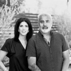 A woman and a man standing outdoors on stairs, smiling at the camera.
