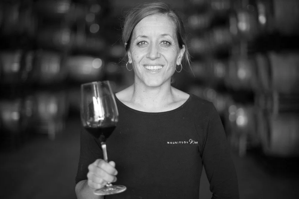 Woman smiling and holding a glass of red wine in a restaurant or bar setting, black and white photo.