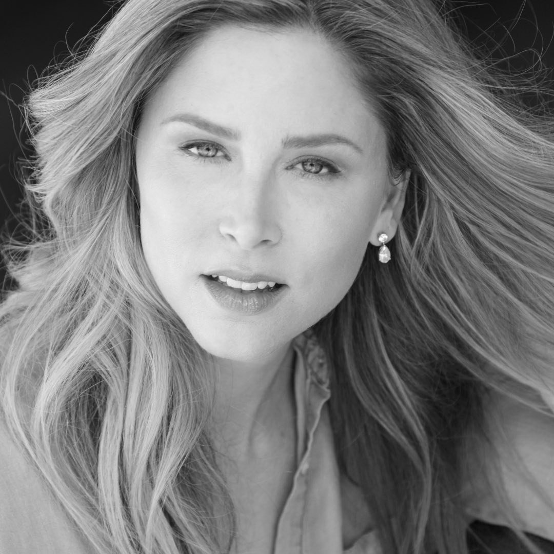 Black and white close-up portrait of a woman with flowing hair, wearing earrings, and looking directly at the camera.