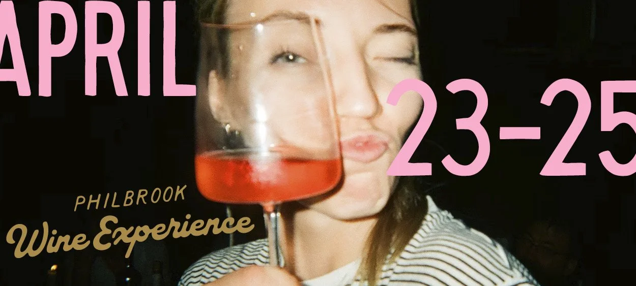 A woman holding a wine glass with pink and orange beverage, winking and puckering her lips, wearing a striped shirt, at the Philbrook Wine Experience event on April 23-25.
