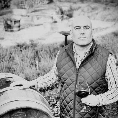 Man holding a glass of red wine standing outdoors near a wine barrel