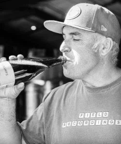 Man with long hair and a cap drinking a bottle of beer