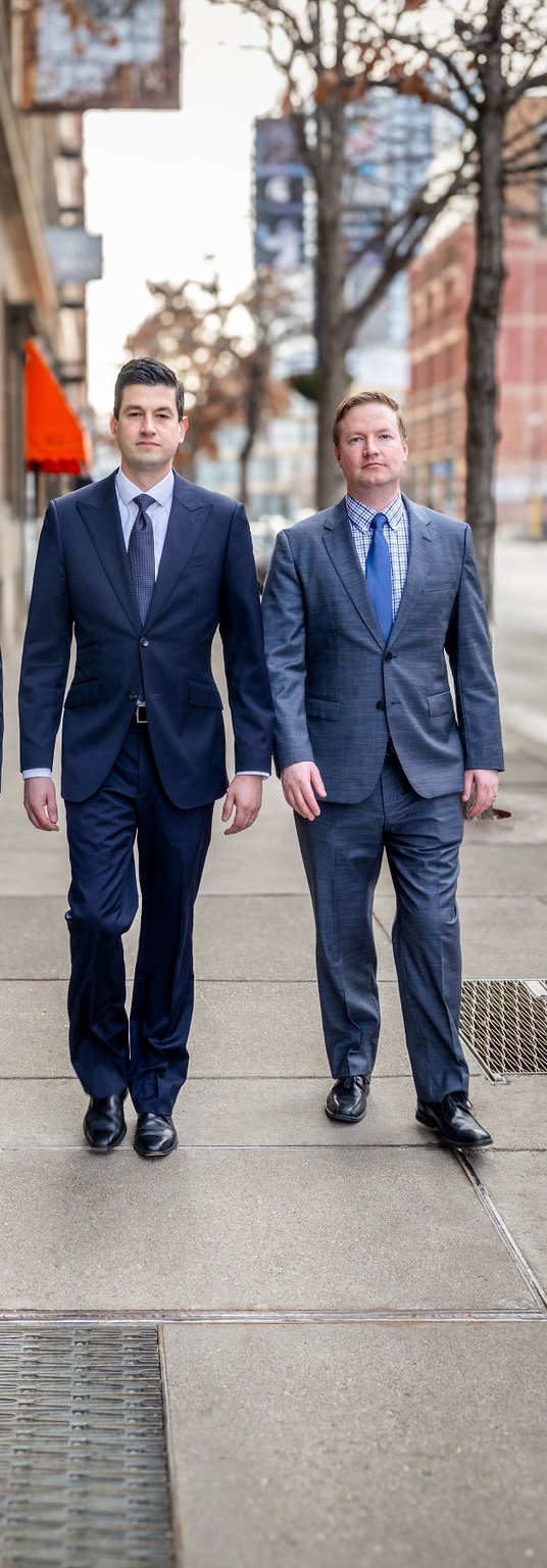 Two men in business suits walking on a city sidewalk.