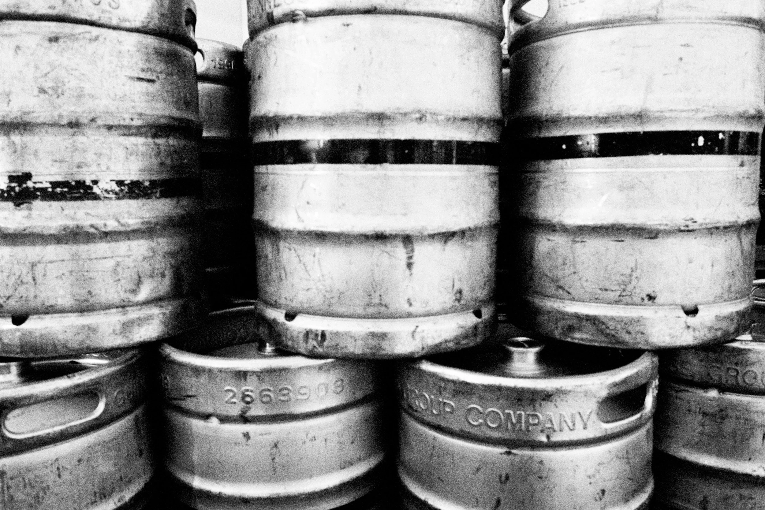 Stacks of metal beer kegs in a black and white photograph.