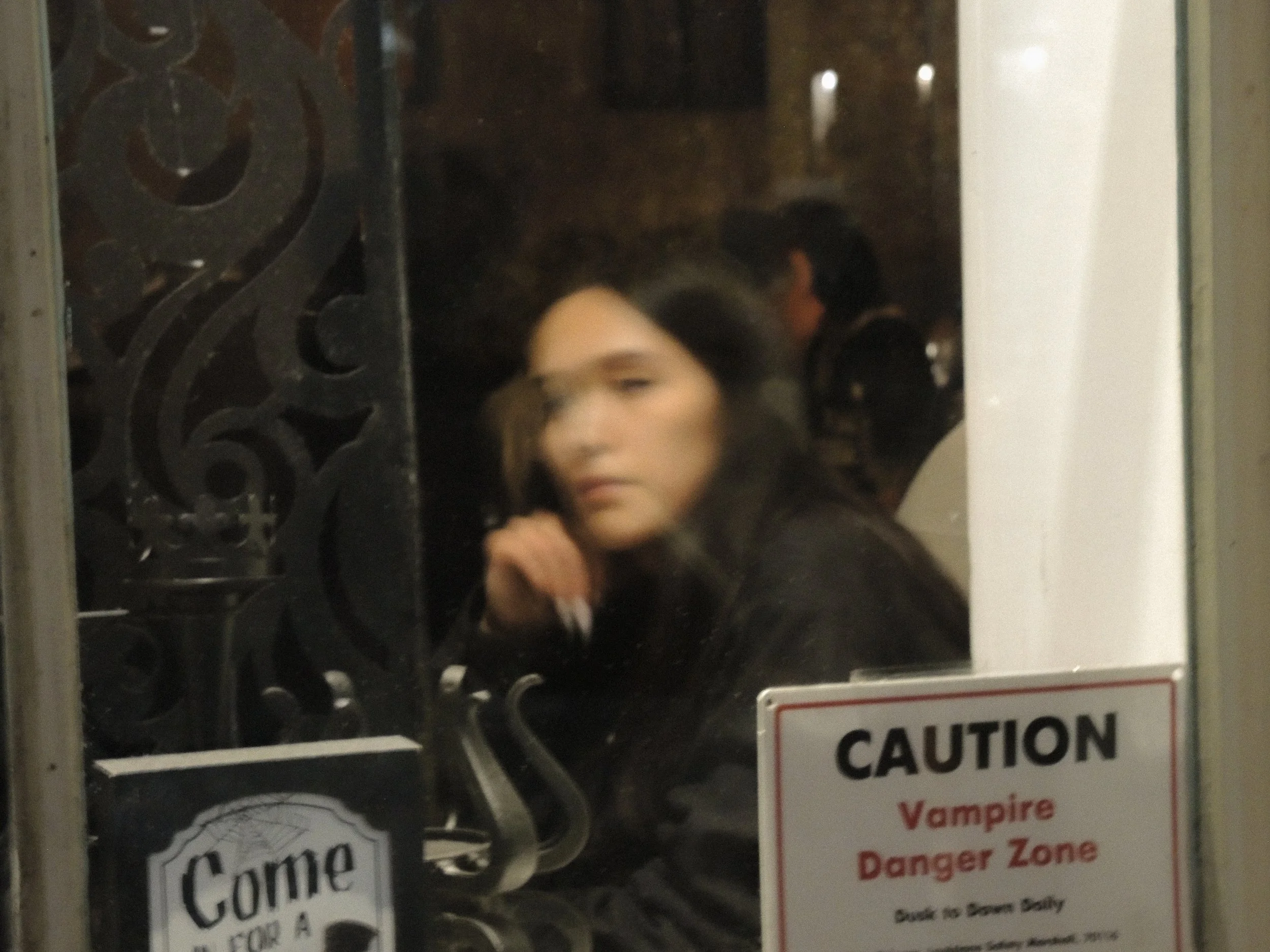 A blurred woman looks through a window. In the window is posted a sign: "Caution: vampire danger zone."