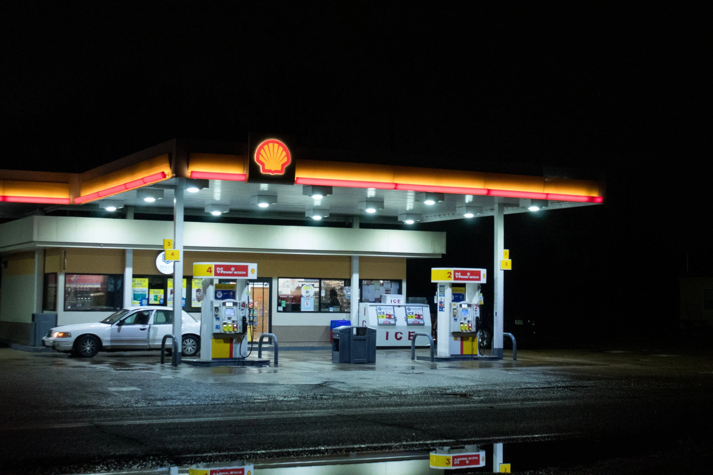 A Shell gas station is illuminated in a pitch-black night.