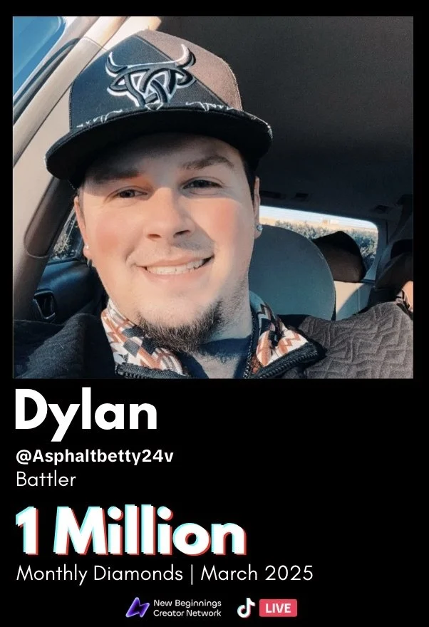 A young man with a beard and mustache smiling in a car, wearing a black baseball cap with a bull logo and a patterned collared shirt.