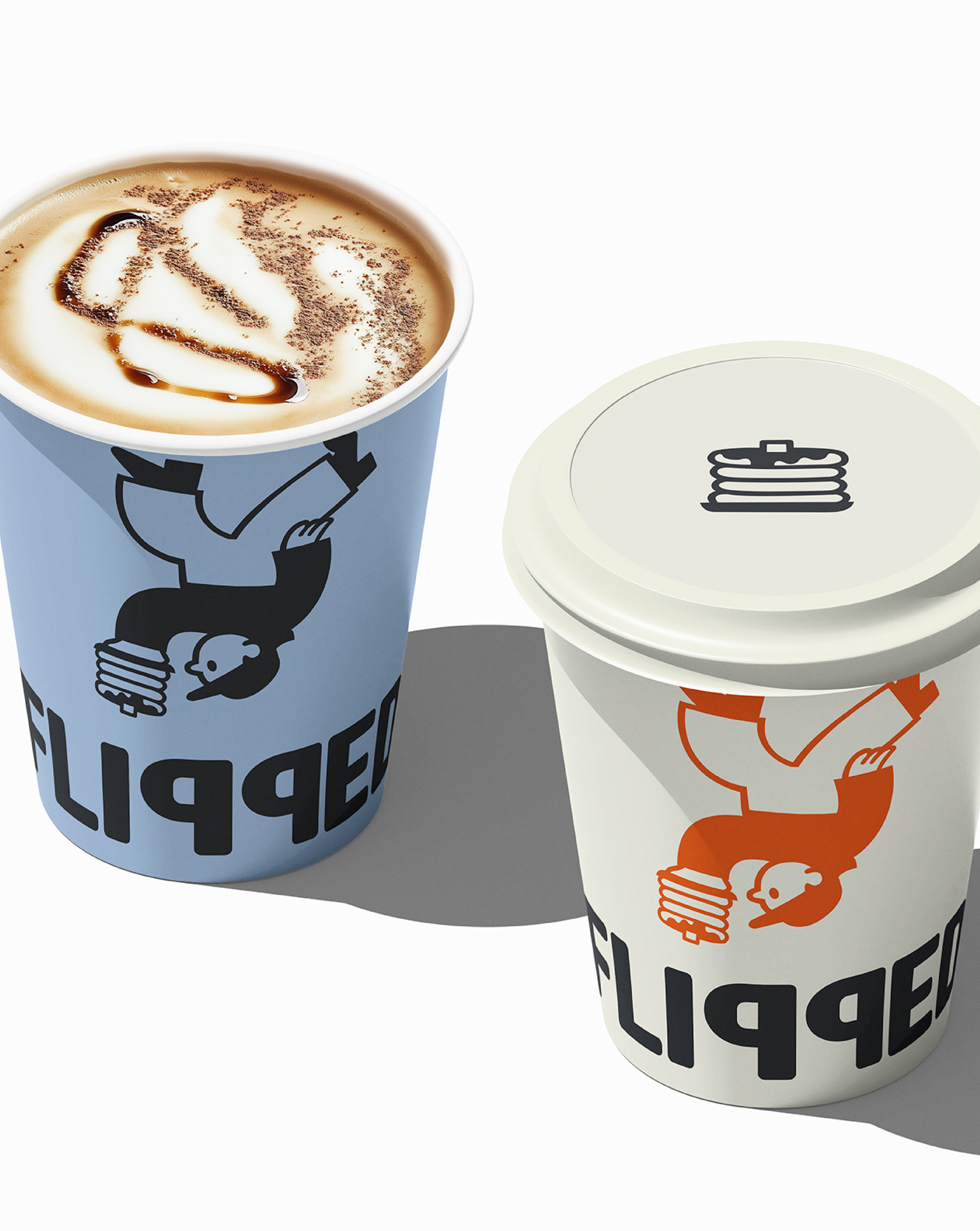 Two disposable coffee cups with spoon and bird logo, one filled with a foam drink topped with cocoa powder, the other sealed with a lid